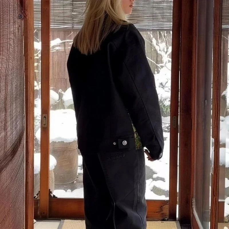 Person wearing a black coat standing inside a building with snow visible outside.